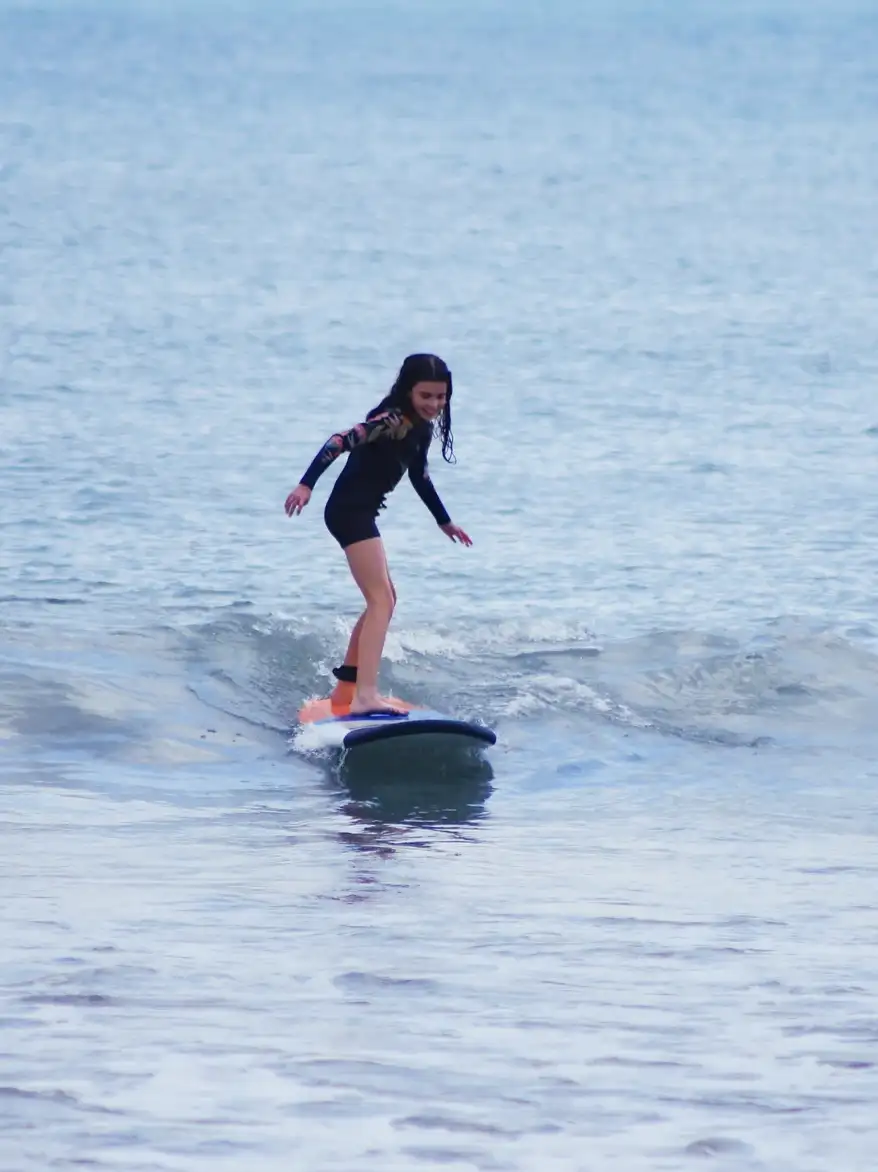 A young surfer riding a soft-top board on a small wave in Bali