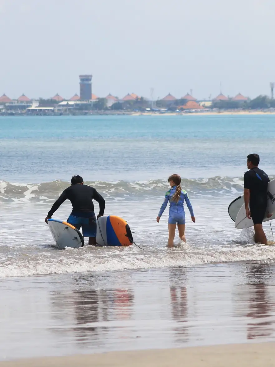 A surf instructor walking a young girl and her surfboard into small waves in Bali